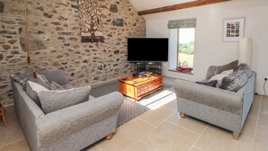 A living room with stone walls, a flat-screen TV, two grey sofas, and a wooden coffee table. - Wern Olau Cottage (Caernarfon)