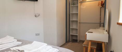 A hotel room with a bed, a TV mounted on the wall, a closet with shelves, and a small table with a chair.