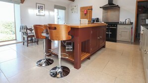 A kitchen with a central island, bar stools, a stove, and a large window. - Wern Olau Cottage (Caernarfon)