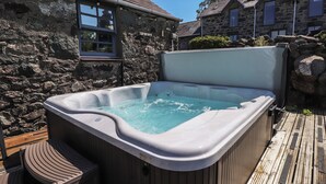 A hot tub with a wooden deck and stone walls. - Wern Olau Cottage (Caernarfon)