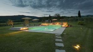Una piscina con cubierta de piedra, rodeada por un césped cuidado y un muro de piedra.