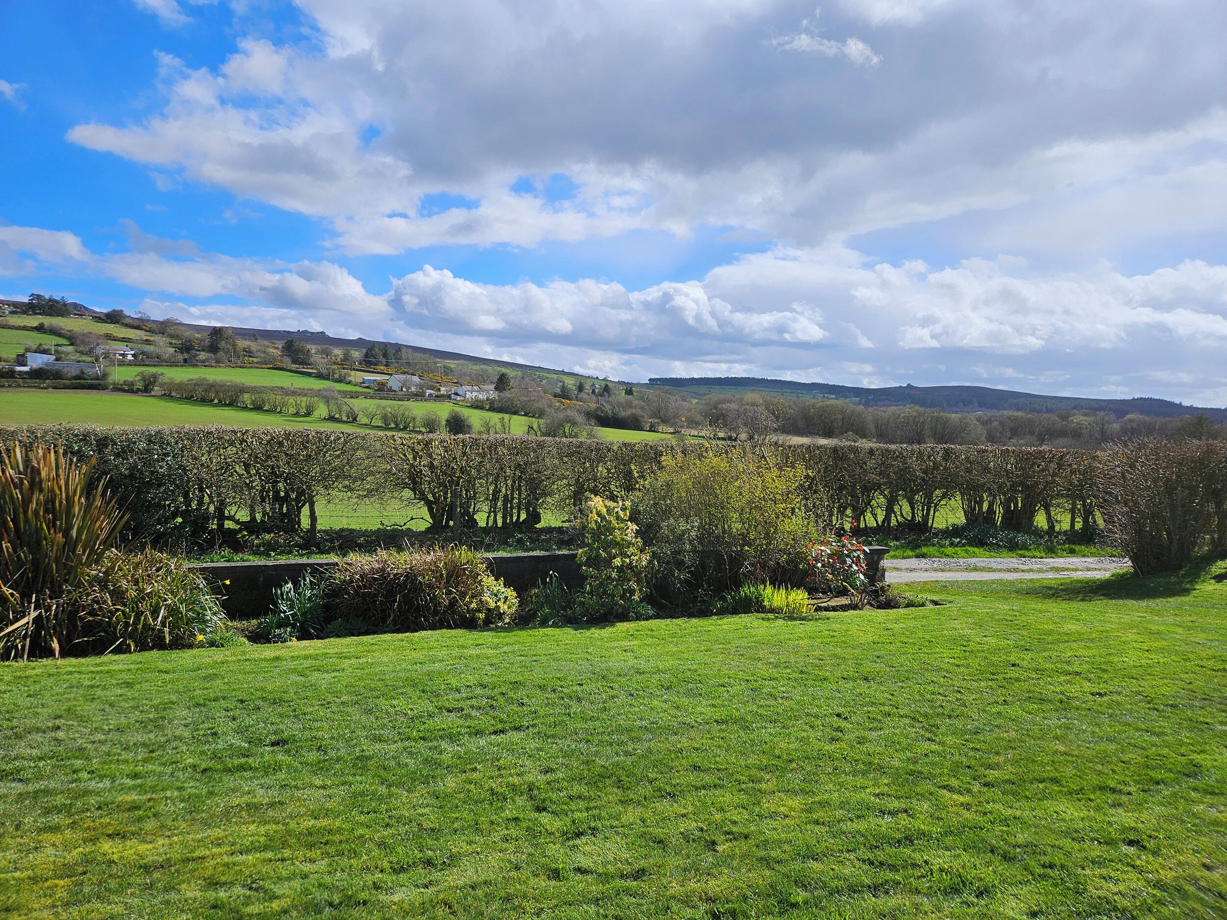 A rural landscape with green fields, a stone wall, and a clear sky.