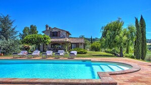 Una villa de piedra con piscina, sillas de descanso y un jardín bien cuidado.