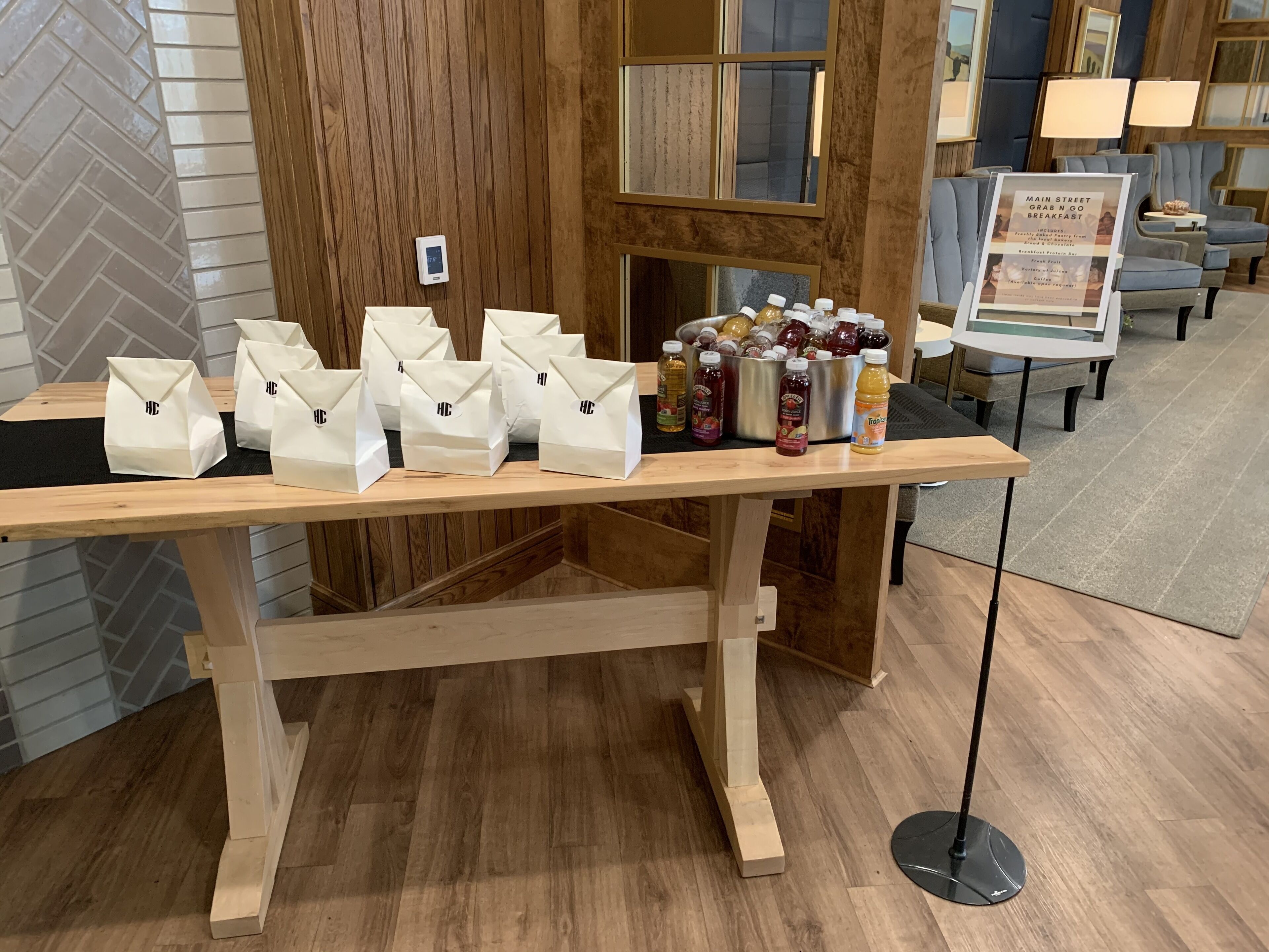 A wooden table with white paper bags and bottles of beverages, likely for sale or as a takeaway option.