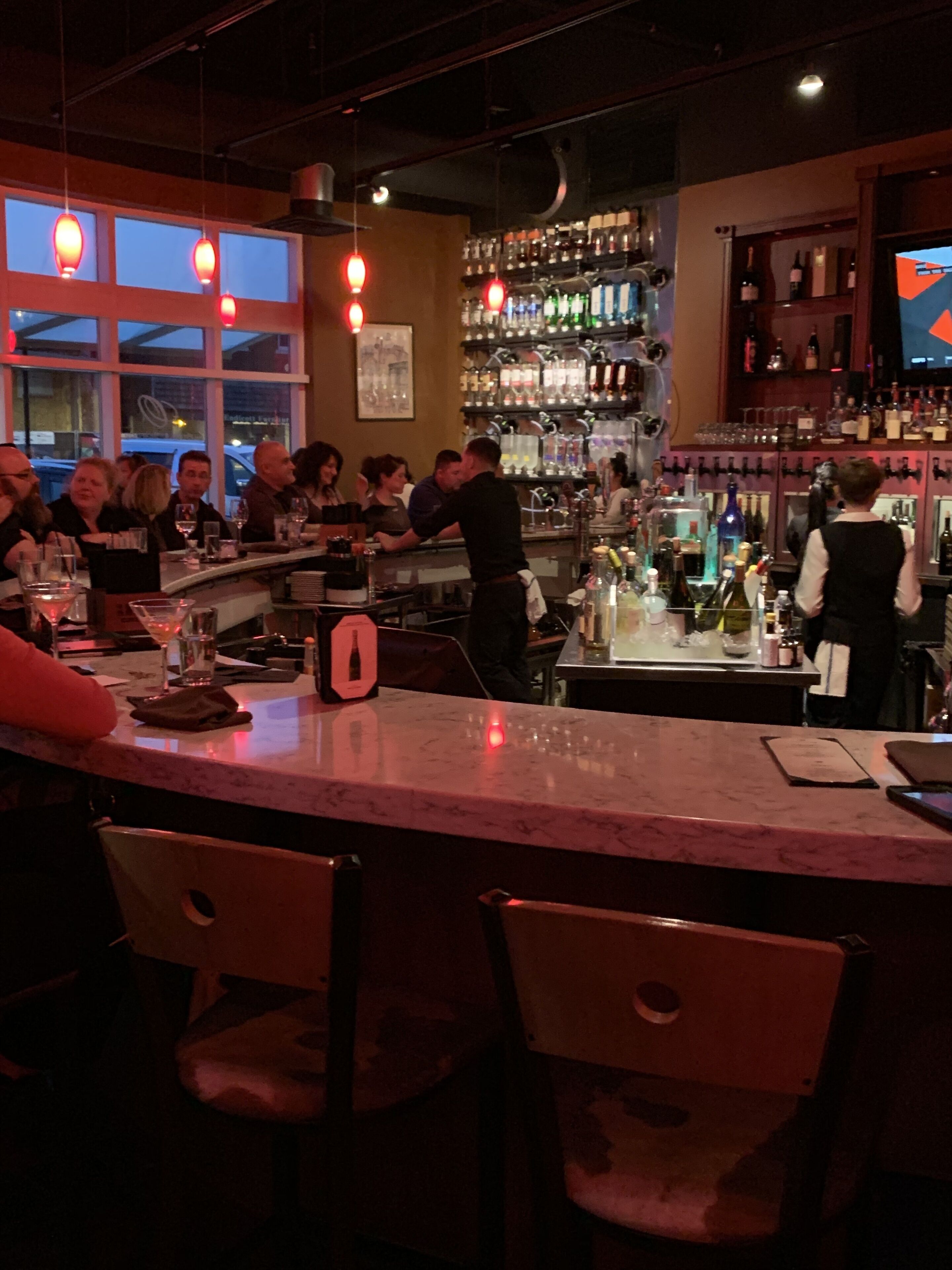 Un espace bar avec un comptoir, des chaises et une variété de bouteilles et de verres disposés sur des étagères.
