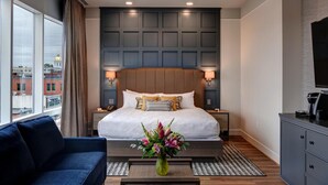 A modern hotel room with a large bed, a blue sofa, a coffee machine, and a view of the cityscape. - The Hotel Concord (Concord)