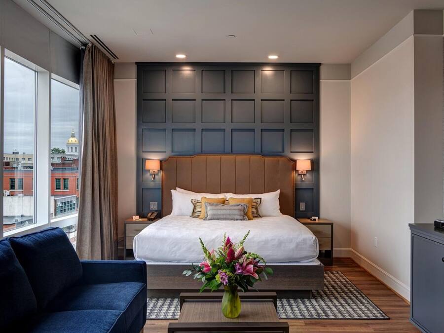 Una habitación de hotel moderna con una cama grande, un sofá azul, una máquina de café y vistas a la ciudad.