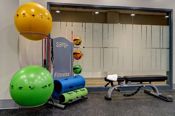 Une salle de sport équipée de ballons d’exercice, d’un banc et d’un support mural pour haltères.