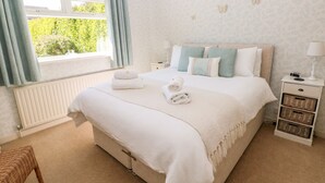 Une chambre à coucher bien aménagée, avec un grand lit, une table de chevet avec une lampe et une vue sur la verdure.