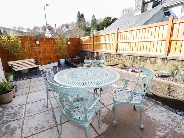A patio with a round table and four chairs, surrounded by potted plants and a wooden fence. - Llwyn Onn (Betws-Y-Coed)