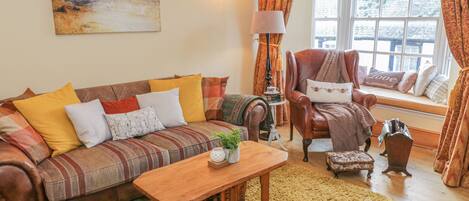 A cozy living room with a striped sofa, a wooden coffee table, a leather armchair, and a window seat with a view.