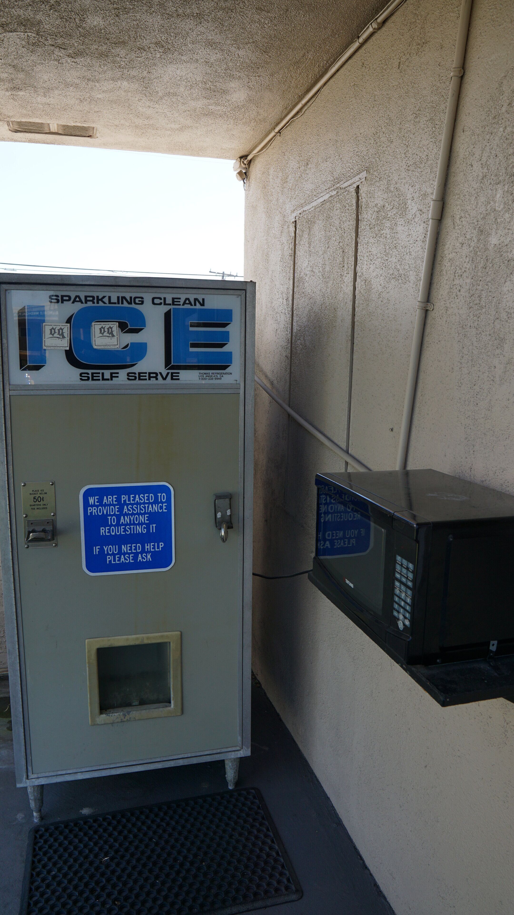 A self-serve ice machine with a sign offering assistance.