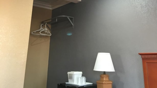 A hotel room with a ceiling painted to resemble clouds, a bed with a red cover, a wooden nightstand with a lamp, and a black storage unit with a white container on top. - Budget Inn (Lawndale)
