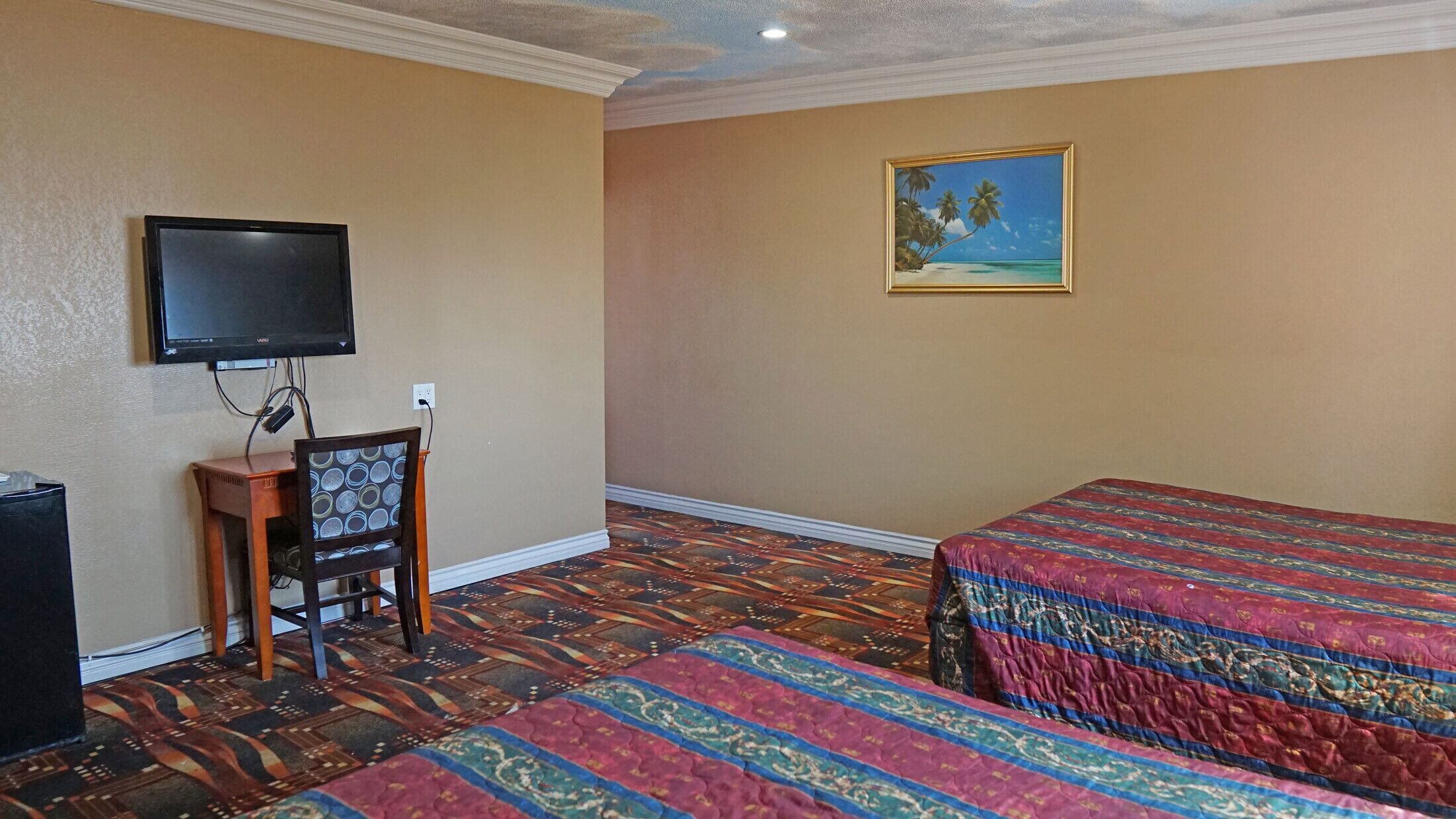 A hotel room with two beds, a television, a small wooden chair, and a painting on the wall.