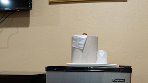 A compact refrigerator with a metallic finish, a small logo on the top, and a white paper towel dispenser on top. - Budget Inn (Lawndale)