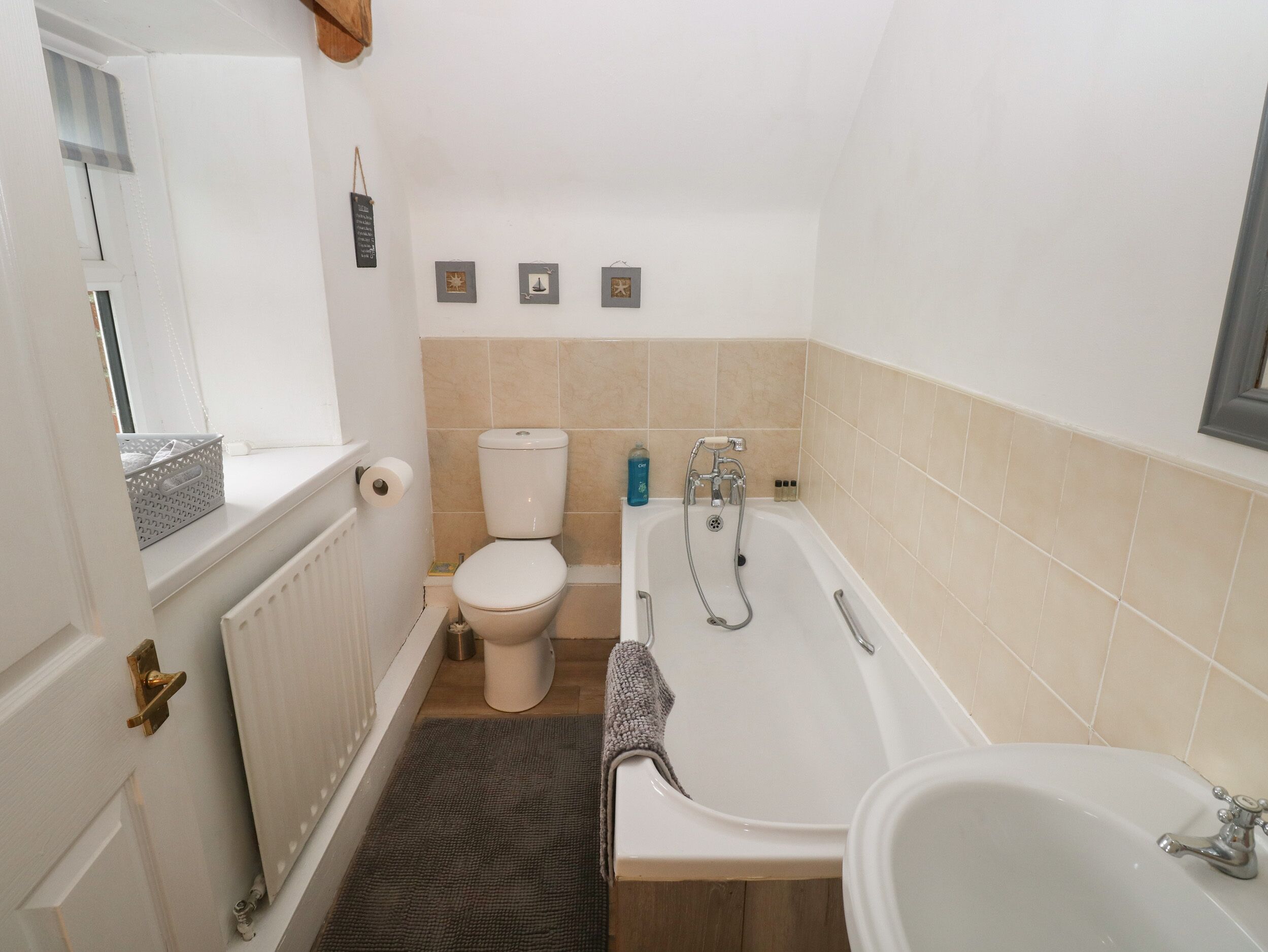Et lille badeværelse med toilet, badekar og et vindue.