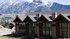 A lodge with a mountain backdrop, featuring a ski lift, stone and wood construction, and large windows.