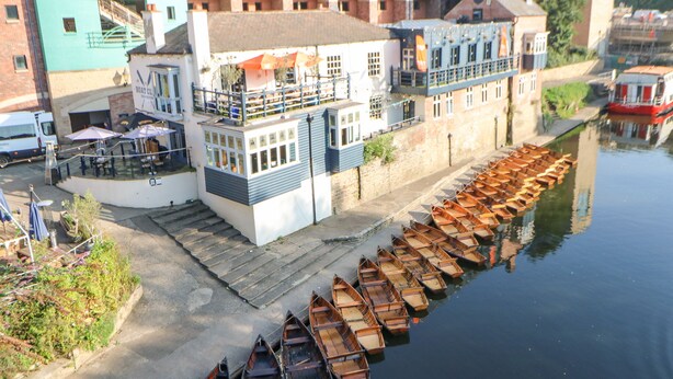 Un edificio a orillas del río con un muelle de barcas de madera.