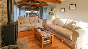 A cozy living room with a fireplace, wooden beams, and a dining area in the background. - The Byre, Sedbury Park Farm (Richmond)