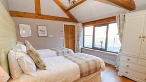 A bedroom with two beds, wooden flooring, a window with curtains, and a white wardrobe. - The Byre, Sedbury Park Farm (Richmond)