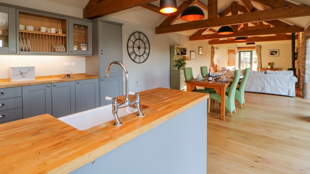 A kitchen with grey cabinets, a wooden countertop, and a sink. There is a dining area with a table and chairs, and a living room with a sofa. - The Byre, Sedbury Park Farm (Richmond)