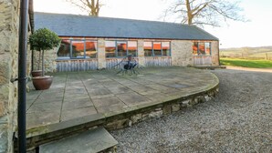 A stone building with a tiled patio, a small table, and a chair. - The Byre, Sedbury Park Farm (Richmond)