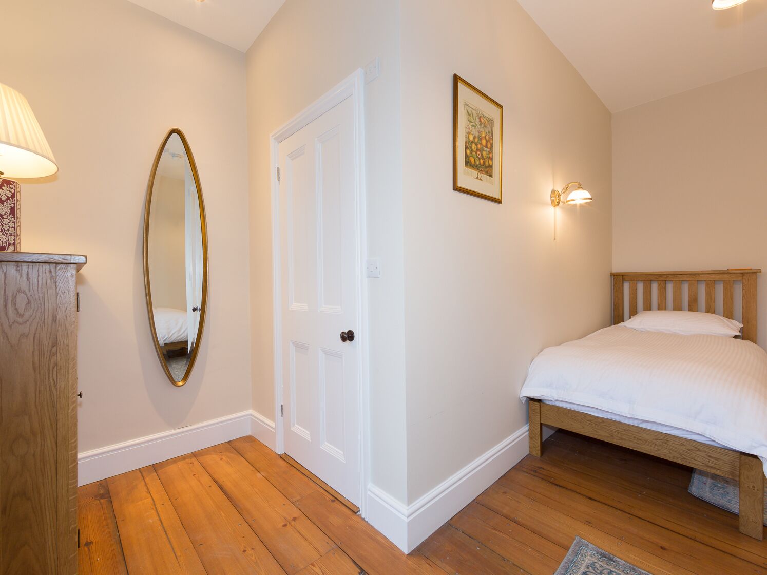 Un dormitorio con cama de madera, puerta blanca, espejo y un cuadro enmarcado en la pared.