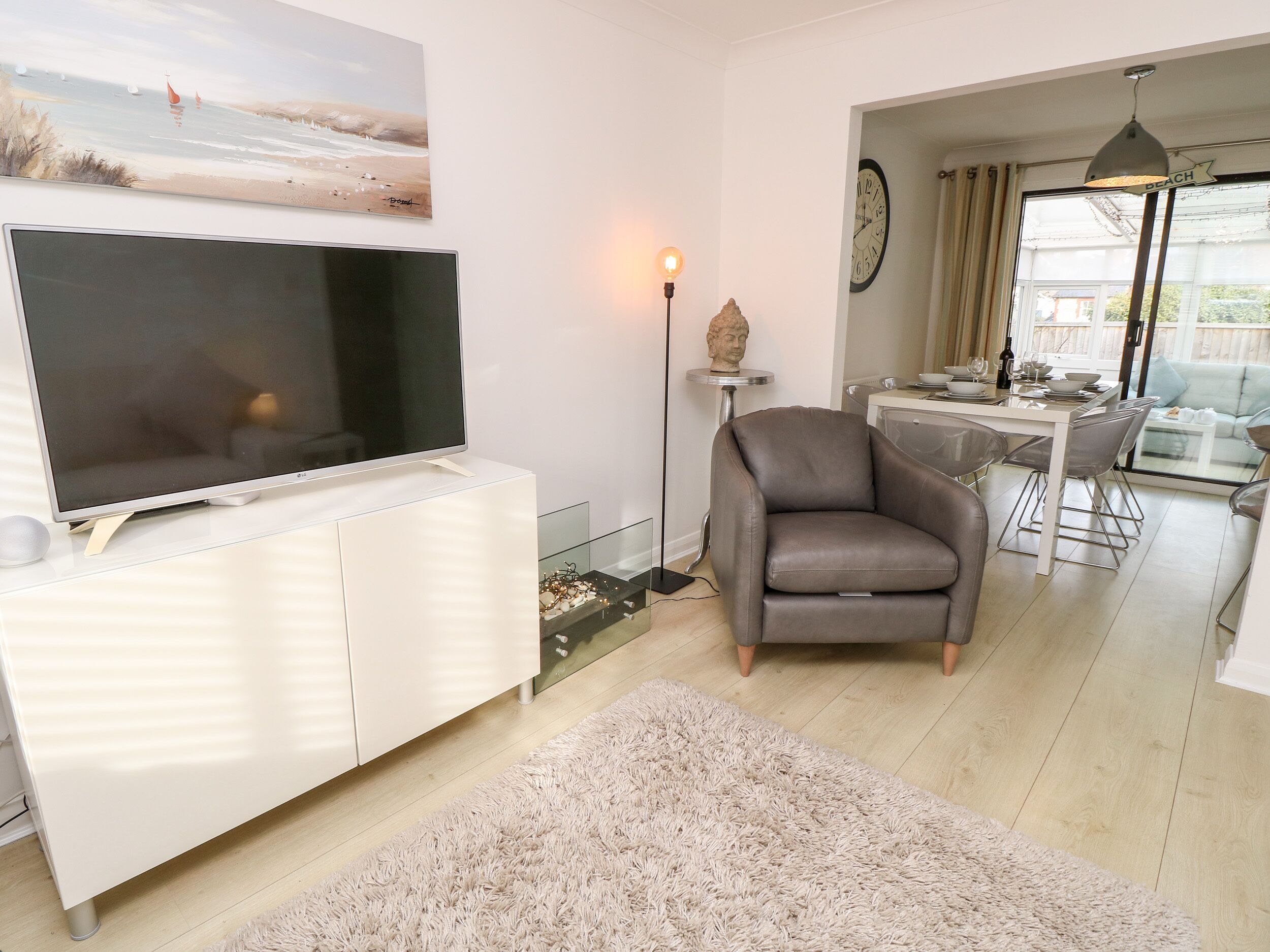 Una sala moderna con un televisor de pantalla plana, un sillón de cuero, una zona de comedor con mesa y sillas, y vistas al exterior a través de una puerta de cristal.