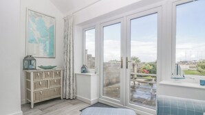 A room with a large sliding glass door leading to an outdoor area, wicker furniture, a blue patterned sofa, and a framed map on the wall. - Driftwood Cottage Roa Island Piel Island (Barrow-in-Furness)