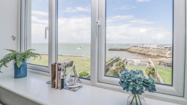 A room with a view of the sea and boats, a potted plant, and a vase with flowers on the windowsill. - Driftwood Cottage Roa Island Piel Island (Barrow-in-Furness)