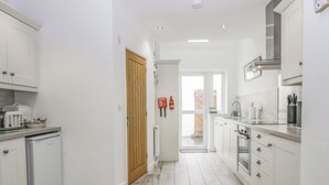 A modern kitchen with white cabinets, a built-in oven, and a small refrigerator. - Driftwood Cottage Roa Island Piel Island (Barrow-in-Furness)