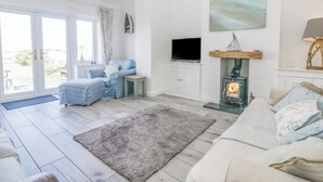 A living room with a sofa, a television, a fireplace, and a large window. - Driftwood Cottage Roa Island Piel Island (Barrow-in-Furness)