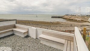 A pebbled beach with a wooden deck and seating area overlooking the sea. - Driftwood Cottage Roa Island Piel Island (Barrow-in-Furness)