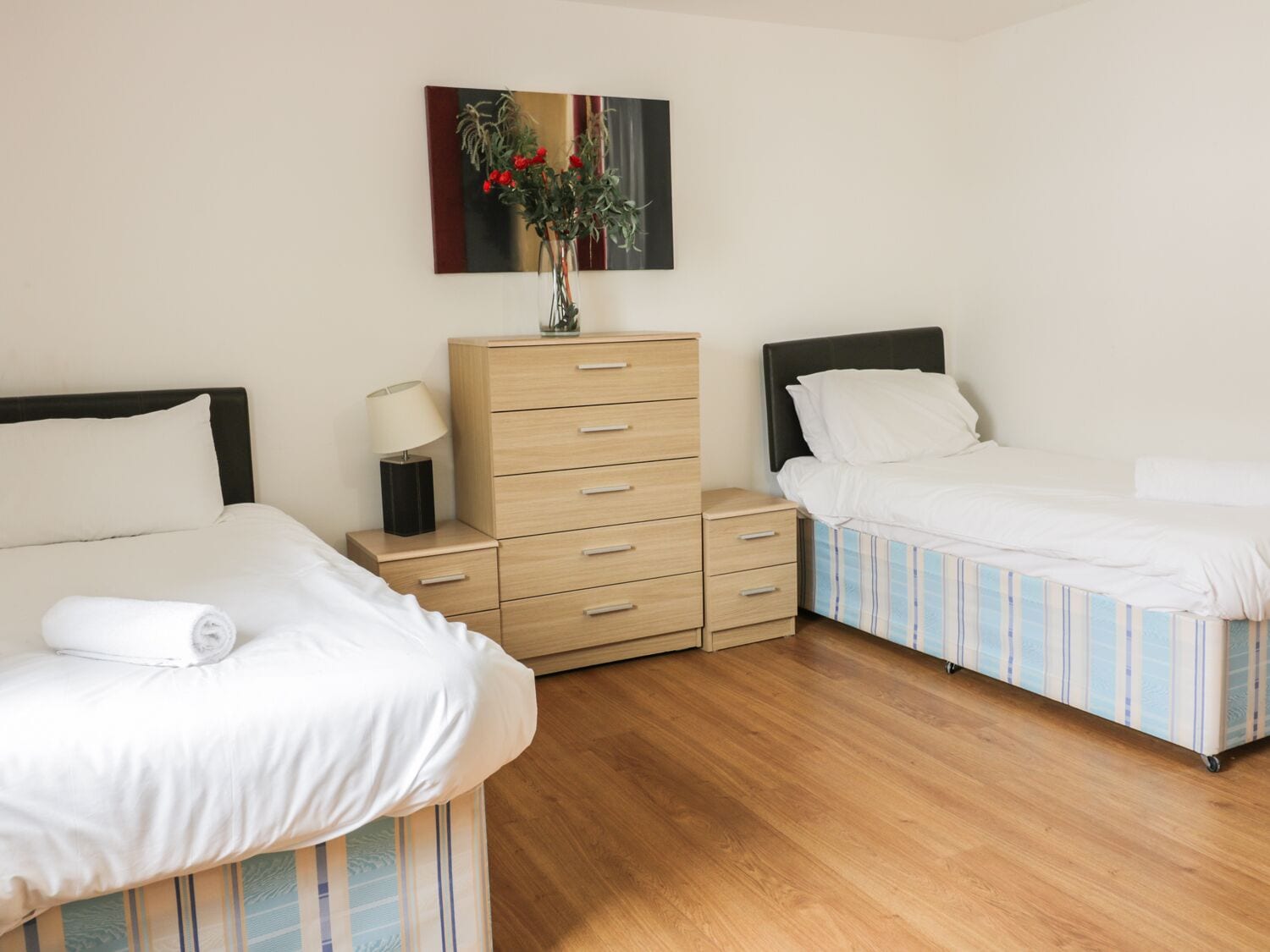A hotel room with two beds, a wooden dresser, a nightstand, and a painting on the wall.