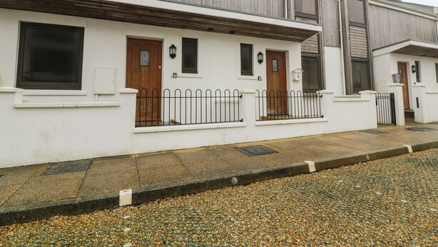 A row of white houses with wooden doors and windows, a gravel driveway, and a metal fence. - 4 Bredon Court (Newquay)