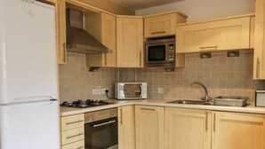 A kitchen with wooden cabinets, a microwave, a stove, and a sink. - 4 Bredon Court (Newquay)