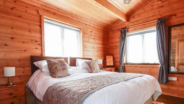 Ein Schlafzimmer einer Holzhütte mit einem großen Bett, zwei Nachttischen, einem Schminktisch und einem Fenster mit Vorhängen.