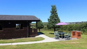 Eine Holzdiele mit einer Veranda, einer Terrasse mit Tisch und Stühlen sowie einem Backofen aus Ziegeln.