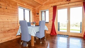 Ein Holzblockbau-Innenraum mit Esstisch, Stühlen und einem Fenster mit Vorhängen.