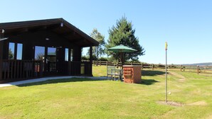 Eine Holzhütte mit Veranda, ein Backsteinbau und ein grüner Sonnenschirm.
