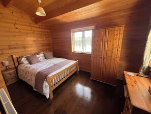 Un dormitorio de cabaña de madera con cama, mesita de noche, armario y ventana.