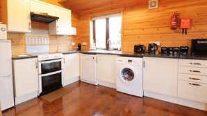 Eine kompakte Küche mit weißen Schränken, einem Backofen, einer Waschmaschine und einer Kaffeemaschine.