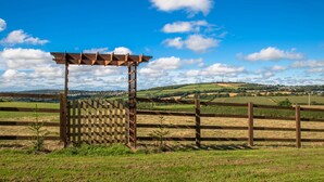 A wooden pergola structure in a rural landscape with a clear blue sky and rolling hills in the background. - Holly Lodge (Bodmin)