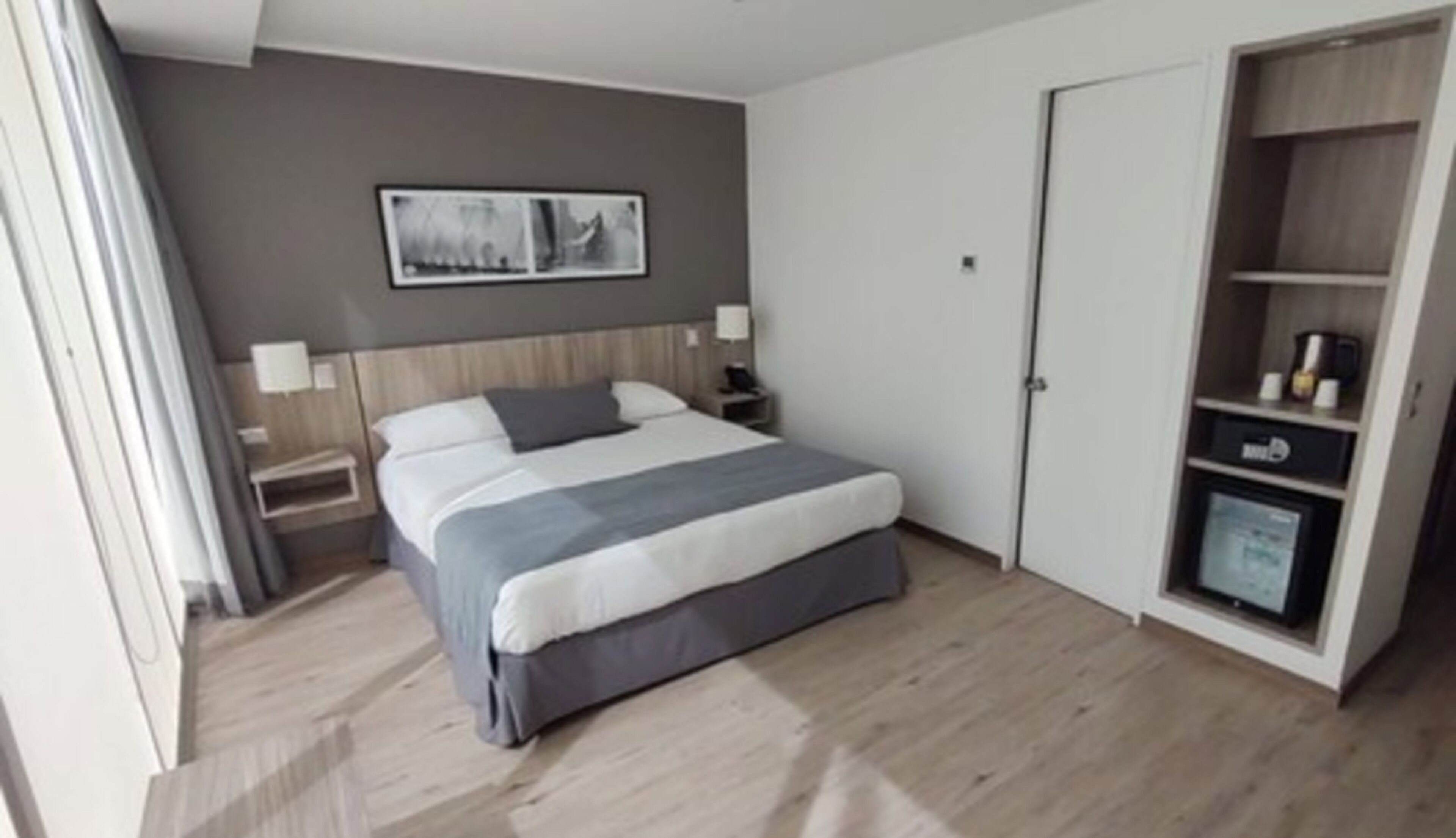 Ein modernes Hotelzimmer mit einem großen Bett, einem Nachttisch mit Lampe, einem Kleiderschrank und einem gerahmten Bild an der Wand.
