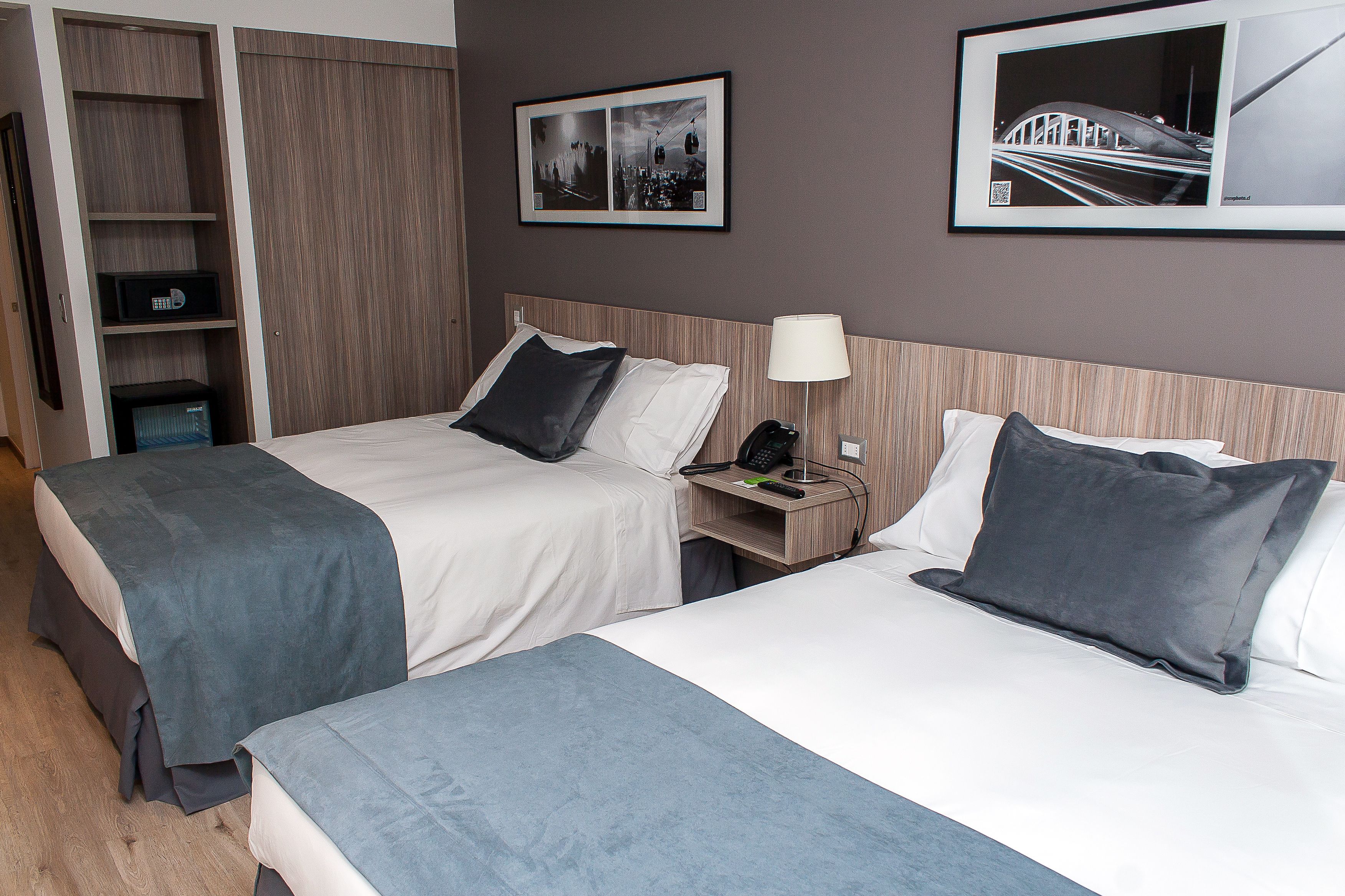 A hotel room with two beds, a nightstand, a lamp, a phone, and a framed picture on the wall.