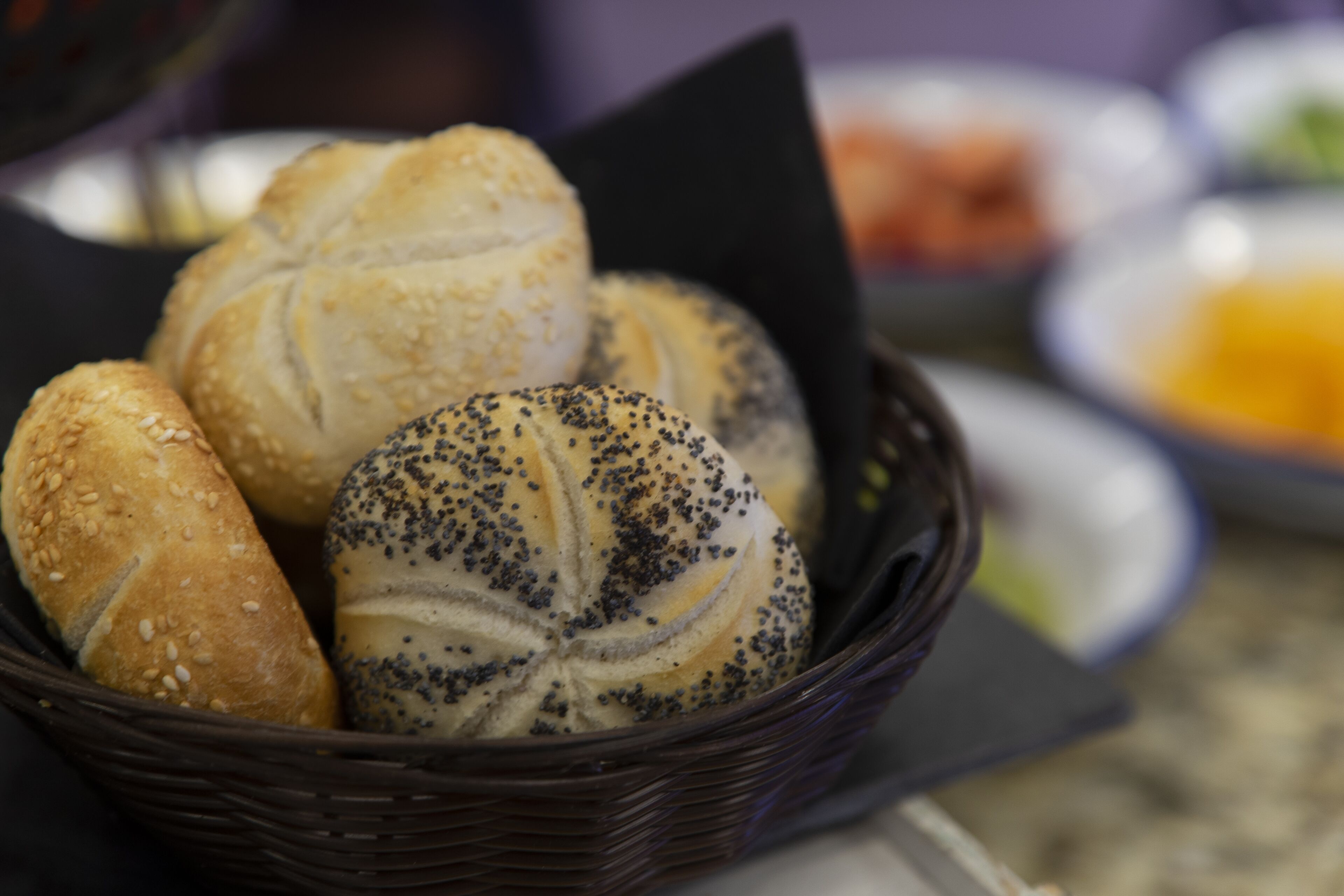 A basket containing various types of bread, including rolls and poppy seed rolls.
