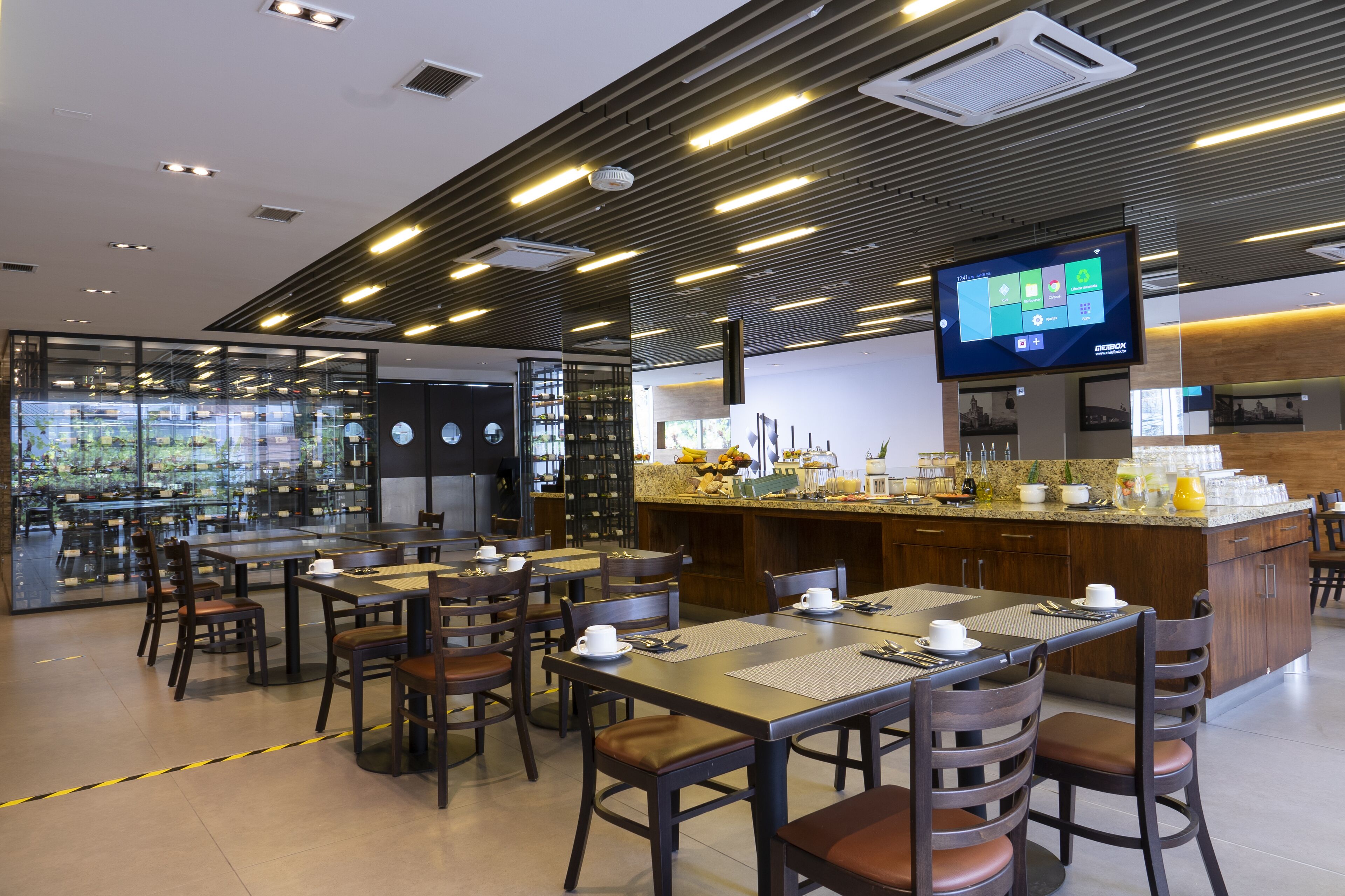 Un restaurante moderno con zona de bar, mesas y sillas de madera y una pantalla digital para el menú.