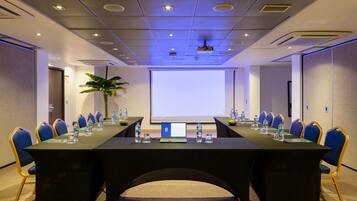 Una sala de conferencias con una larga mesa, sillas azules, botellas de agua y un ordenador portátil.