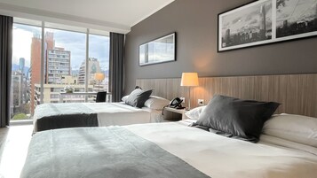 A hotel room with two beds, a city view, a framed picture on the wall, and a lamp on the nightstand.