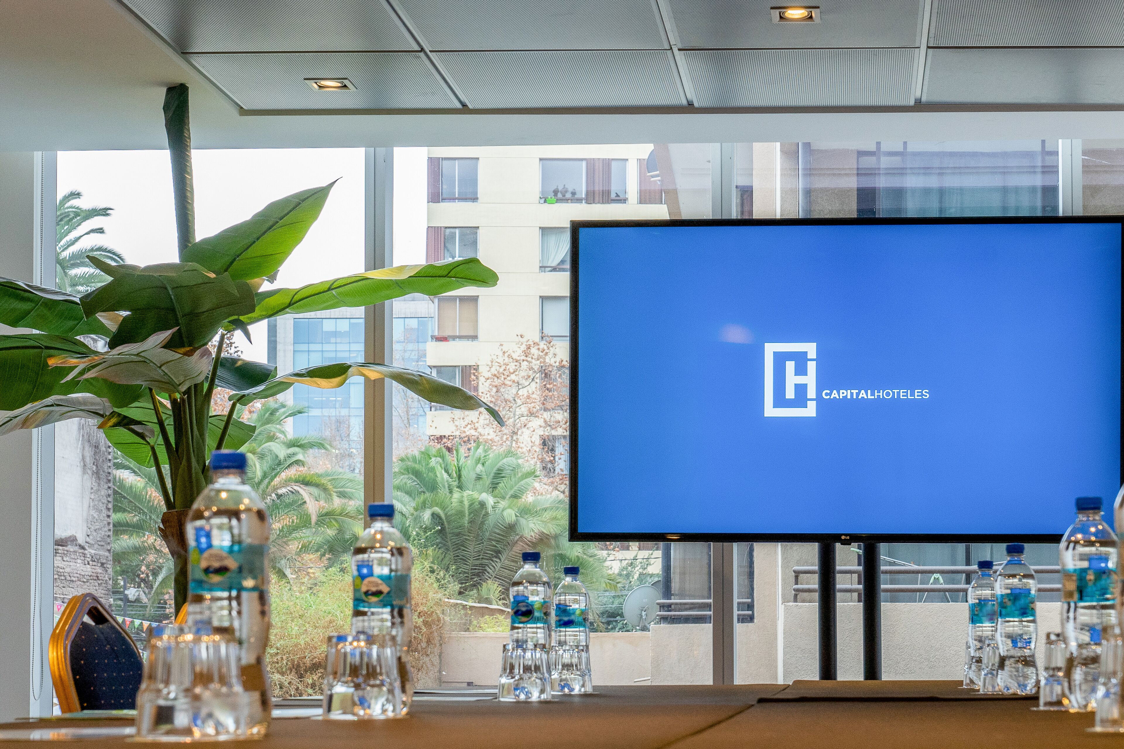 A hotel lobby with a large screen displaying the hotel name, water bottles on a table, and a large plant.